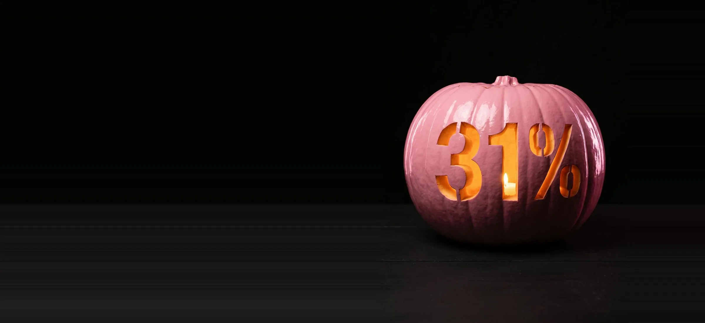 A pink pumpkin carved with 31%, lit by a candle inside