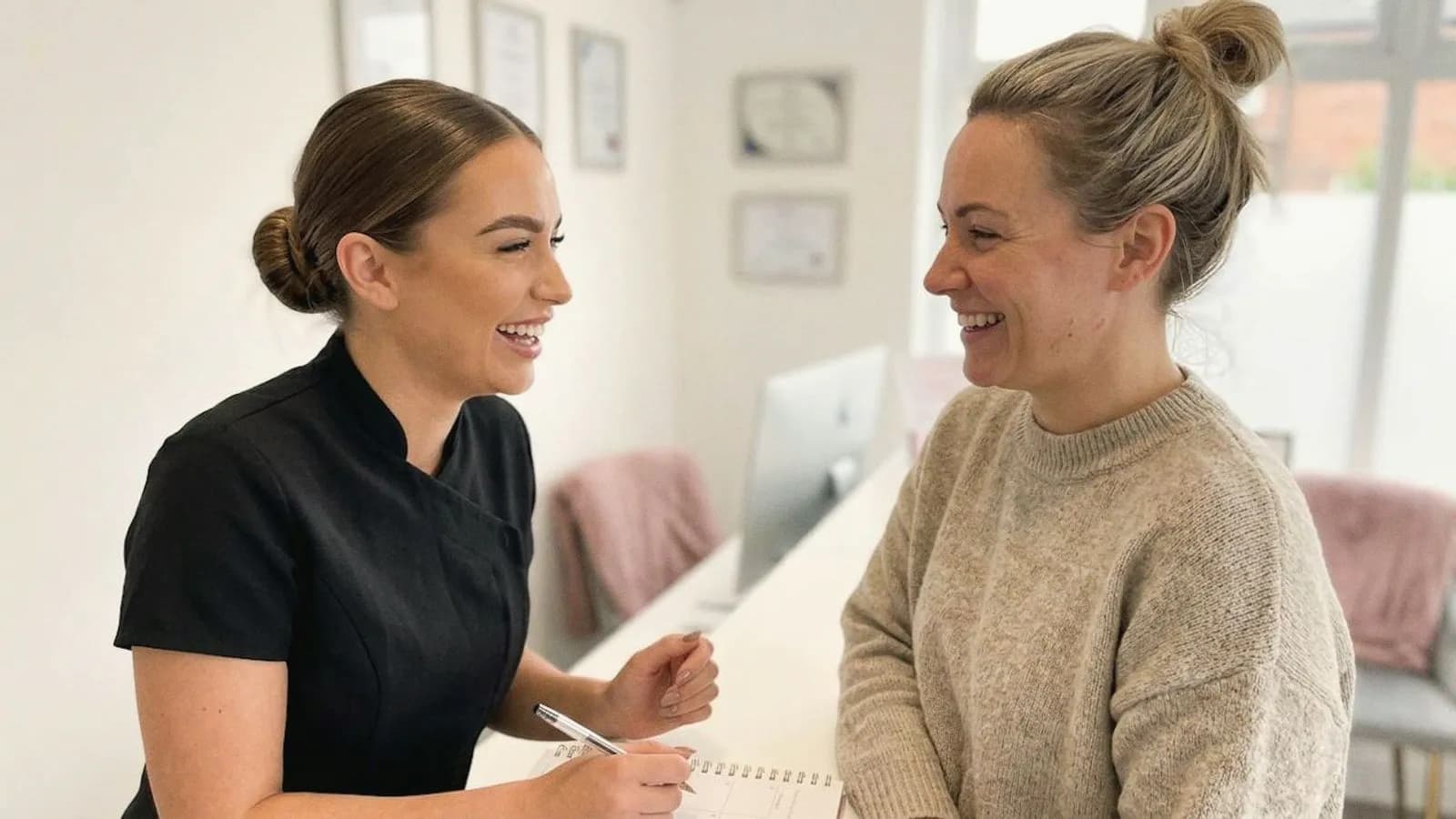 A practitioner and client laugh together at the clinic reception desk.